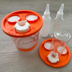 Peut inclure: Un récipient en plastique transparent pour mouches des fruits aptères avec un couvercle orange marqué Model S Patent Pending. L'ensemble comprend deux couvercles orange supplémentaires, deux flacons souples transparents et des filtres blancs.
