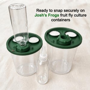 Peut inclure: Deux r&eacute;cipients en plastique transparent avec des couvercles vert fonc&eacute;, chacun dot&eacute; de deux inserts circulaires blancs et d'une ouverture centrale filet&eacute;e. Un r&eacute;cipient a une bouteille transparente fix&eacute;e. Texte : Ready to snap securely on Josh's Frogs fruit fly culture containers.
