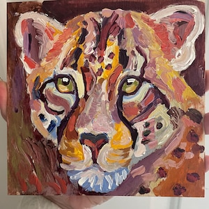 May include: Square painting of a cheetah's face. The artwork uses thick brushstrokes and a palette of orange, yellow, purple, and brown. The cheetah's eyes are green, and the background is a dark brown.