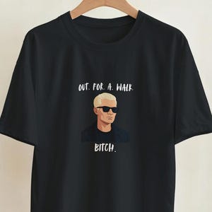 Könnte beinhalten: Ein schwarzes kurzärmeliges T-Shirt mit einer grafischen Illustration einer Person mit blonden Haaren und schwarzer Sonnenbrille. Der Text über der Illustration lautet OUT. FOR. A. WALK. und unter der Illustration steht BITCH.