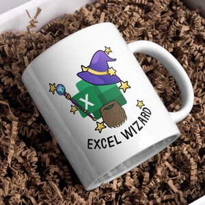 Puede incluir: Taza de cerámica blanca con un diseño caprichoso de "Excel Wizard". El diseño presenta un sombrero de mago morado, un icono verde de Excel, una barba marrón, una varita mágica y acentos de estrellas. La taza está en una caja con papel marrón.