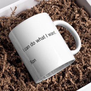 Puede incluir: Una taza de cerámica blanca con el texto impreso en negro I can do what I want. seguido del nombre Ron en el lateral. La taza tiene un cuerpo cilíndrico liso y un asa curva, presentada con un diseño limpio y sencillo para uso diario.