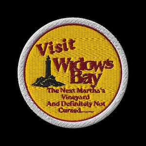 May include: A circular embroidered patch with a yellow background and a white border. It features a black lighthouse silhouette and red text that reads: Visit Widow's Bay, The Next Martha's Vineyard And Definitely Not Cursed.