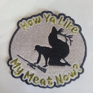May include: Embroidered patch with the text "How Ya Like My Meat Now?" in a green and yellow font. The patch features a black silhouette of a chicken and a person with a rifle. The patch has a gray background and a dark blue border.