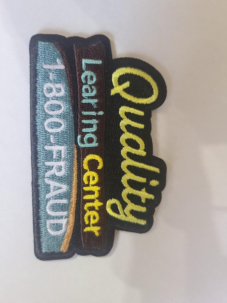 May include: Embroidered patch with the words "1-800-FRAUD", "Learning Center", and "Quality". The patch has a black border, with the text in various colors including blue, yellow, and brown. The patch is rectangular with a curved edge.
