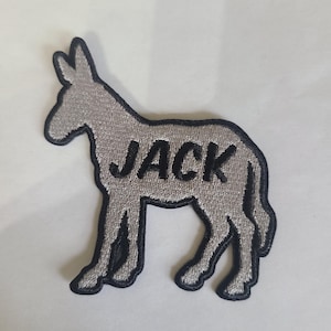 May include: A gray donkey patch with the name "JACK" embroidered in black. The patch has a black outline and is likely for clothing or accessories. The donkey is in a standing profile.