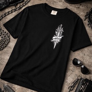 May include: Black t-shirt featuring a detailed white graphic of a sword engulfed in flames, with a banner that reads "DON'T GIVE UP." The design is centered on the front of the shirt. The shirt is made of a soft material.