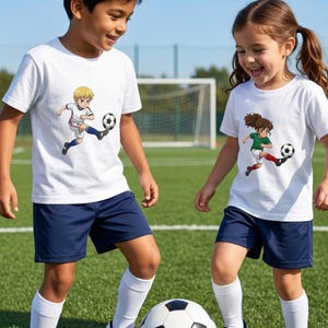 Puede incluir: Dos ni&ntilde;os con camisetas blancas con gr&aacute;ficos de f&uacute;tbol y pantalones cortos azul marino juegan al f&uacute;tbol en un campo verde. Las camisetas presentan ilustraciones de dibujos animados de futbolistas. Llevan calcetines blancos y zapatillas deportivas blancas y negras. Hay un bal&oacute;n de f&uacute;tbol.