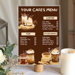 May include: A clear acrylic cafe menu with a wooden base displays a menu with coffee, tea, and other drinks. The menu features watercolor illustrations of beverages and the text "YOUR CAFE'S MENU". A white candle and a decorative lantern are in the background.