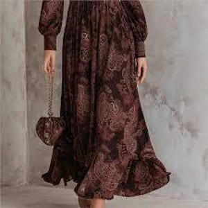 May include: A long, brown dress with a paisley pattern and long sleeves. The dress has a pleated skirt and a ruffled hem. A matching brown purse with a chain strap is held in the hand.