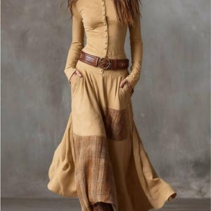 Könnte beinhalten: Ein beigefarbenes Kleid mit langen Ärmeln und einer Knopfleiste vorne. Das Kleid hat einen braunen Ledergürtel mit dekorativer Schnalle und Taschen. Der Rock hat Karopatchs. Das Kleid ist aus einem weichen, fließenden Stoff gefertigt.