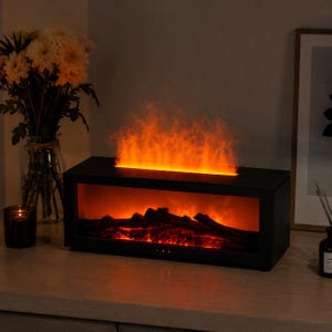 May include: A black electric fireplace with a realistic flame effect. The rectangular unit features glowing embers and a simulated flame rising from the top. The fireplace is placed on a wooden surface, with a vase of flowers and a candle in the background.