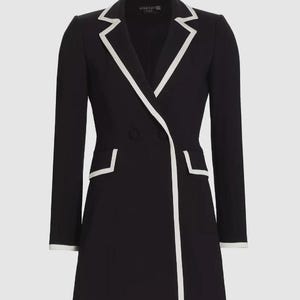 Puede incluir: Un vestido blazer negro con ribetes blancos en las solapas, bolsillos y dobladillo. El diseño cruzado presenta dos botones y mangas largas. El vestido tiene un corte entallado y un estilo clásico y elegante.