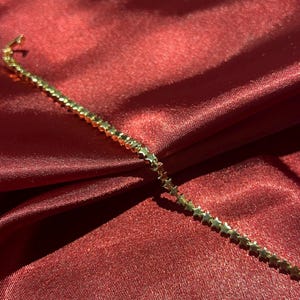 Pode incluir: Uma pulseira de corrente em tom dourado com uma série contínua de pequenos elos uniformes em forma de estrela. Os elos metálicos estão ligados em linha reta, criando um padrão delicado e repetitivo ao longo da peça de joalharia.