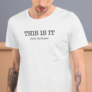 Puede incluir: Camiseta blanca con el texto "THIS IS IT" en negrita, en negro, con "Murder, She Recapped" debajo en una fuente más pequeña. La camiseta es de manga corta y cuello redondo.