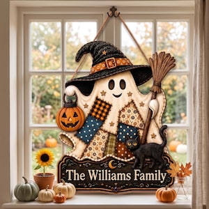 May include: A decorative wall hanging featuring a ghost wearing a black witch hat, holding a jack-o'-lantern and a broom. The ghost has patchwork patterns and a black cat stands on a base with the text The Williams Family printed in white.