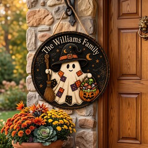 May include: A round wooden sign featuring a ghost wearing a witch hat and holding a broom and a pumpkin basket filled with skulls and mushrooms. The text reads The Williams Family. The background is black with spiderwebs, stars, and moons.