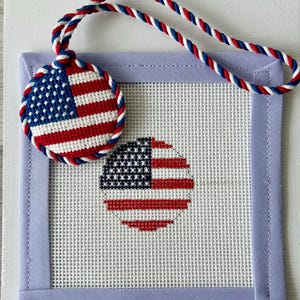 May include: A patriotic needlepoint ornament and canvas featuring the American flag. The round ornament and the flag design on the canvas are stitched in red, white, and blue. A matching twisted cord serves as a hanger. The canvas is framed with a light blue border.