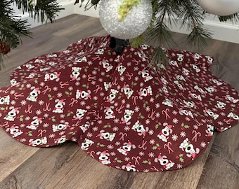May include: A circular Christmas tree skirt in a deep maroon fabric featuring a repeating pattern of white cartoon dogs wearing red Santa hats, interspersed with small white snowflakes, green holly leaves, and red and white candy canes.