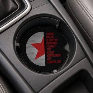 May include: A circular car cup holder coaster featuring a split design. The left side displays a red star on a light gray background with geometric lines. The right side is black with the red text: LONGING, RUSTED, SEVENTEEN, DAYBREAK, FURNACE, NINE, BENIGN, HOMECOMING, ONE, FREIGHT CAR.