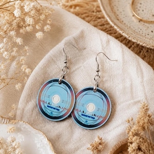 Peut inclure: Une paire de boucles d'oreilles pendantes circulaires arborant une impression graphique bleu clair de la pochette de l'album Millennium des Backstreet Boys. Chaque boucle possède un crochet en métal argenté et un anneau de jonction.