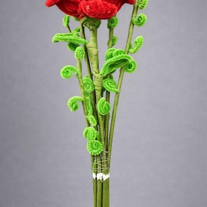 May include: A handcrafted bouquet of flowers made from red and green pipe cleaners. The large flower at the top is red, and the stems and leaves are green. The stems are bound with wire and white tape.