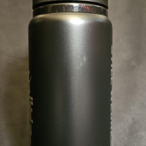 May include: Black insulated water bottle with a flip-top lid. The bottle has a matte finish and a cylindrical shape. Text is visible on the side. Ideal for sports, travel, or everyday hydration.