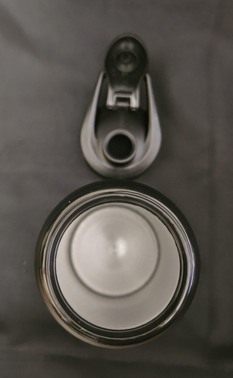 May include: An overhead shot of a stainless steel tumbler with a black rim and a matching lid. The lid is open, revealing the interior of the tumbler. The background is a solid gray.