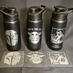 May include: Three black water bottles with silver designs and matching coasters. The bottles feature images of a helmet, a character, and the text "THIS IS THE WAY". The coasters have the same designs. The bottles are approximately 9 inches tall.