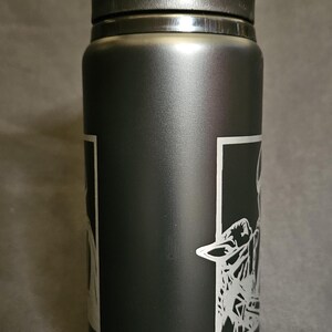 May include: Black insulated water bottle with a black flip-top lid. The bottle features a white graphic design on the side. The text "WED" is visible below the graphic. This reusable bottle is designed for hydration.
