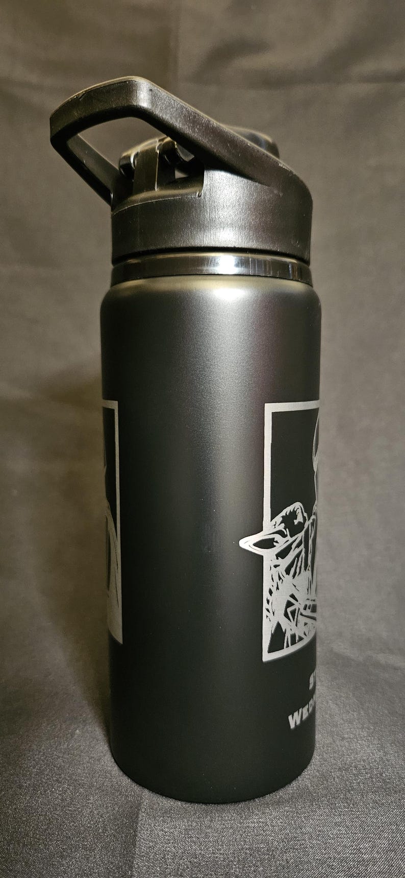 May include: Black insulated water bottle with a black flip-top lid. The bottle features a white graphic design on the side. The text "WED" is visible below the graphic. This reusable bottle is designed for hydration.