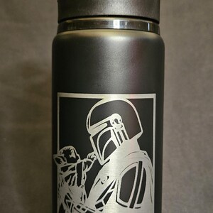 May include: Black water bottle with a flip-top lid. The bottle features a silver graphic of a Mandalorian and Grogu, with the text "STILL WEDNESDAY" below the graphic. The bottle is designed for cold beverages.