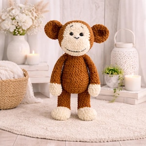 May include: A handmade, plush monkey toy with a brown body, cream-coloured face, ears, hands, and feet. The monkey has black eyes and a stitched smile. The toy is standing on a cream-coloured rug.