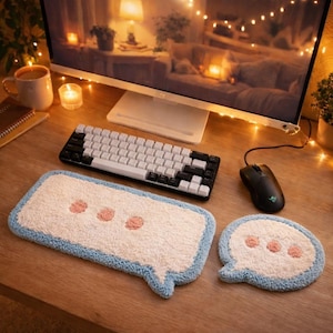 May include: A desktop setup featuring a white and black mechanical keyboard, a black mouse, and two speech bubble-shaped rugs. The rugs are white with pink dots and a light blue border. A computer monitor and a mug are also visible.