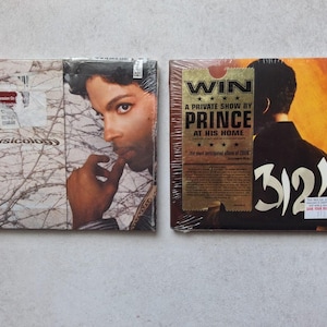 May include: Two sealed music CDs. The left cover features a portrait of Prince with the text Musicology and a red sticker. The right cover is orange and black with the text 3121 and a gold sticker that reads WIN A PRIVATE SHOW BY PRINCE AT HIS HOME.
