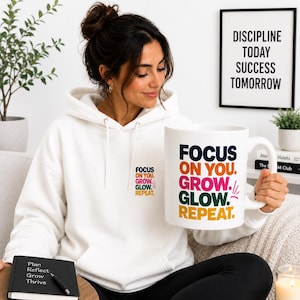 以下が含まれることがあります： モチベーションテキスト入りの白いパーカーとマグカップ。パーカーには「FOCUS ON YOU. GROW. GLOW. REPEAT.」とプリントされています。マグカップにはカラフルなテキストで「FOCUS ON YOU. GROW. GLOW. REPEAT.」と書かれています。