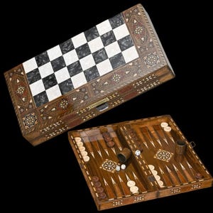 May include: A wooden backgammon board game set featuring a closed case with a black and white checkered top and an open board interior with dark and light wooden points, circular game pieces, two dice cups, and two dice with inlaid geometric patterns.