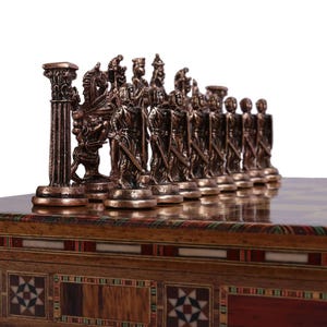 Può includere: Un set di scacchi in bronzo con pezzi dettagliati, tra cui cavalieri e soldati, su una scacchiera in legno. La scacchiera è posta su una scatola di legno decorativa con motivi intarsiati. I pezzi degli scacchi sono alti circa 7.6 cm.