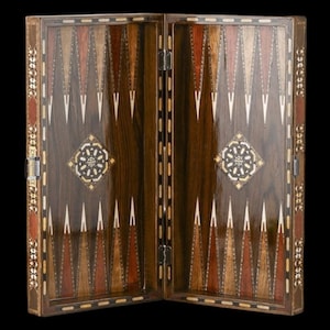 Peut inclure: Un plateau de backgammon en bois avec une finition brun foncé polie et des pointes triangulaires incrustées dans des tons de bois alternés clairs et foncés. Le centre de chaque côté présente un motif en étoile géométrique avec des accents de nacre.