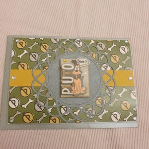 Könnte beinhalten: Handgefertigte Grußkarte mit einer Cartoon-Hundeillustration. Die Karte hat einen grünen Hintergrund mit Knochen- und "P"-Symbolen, einen gelben Streifen und ein zentrales Ausschnittdesign. Der Hund sagt "Snack?!"