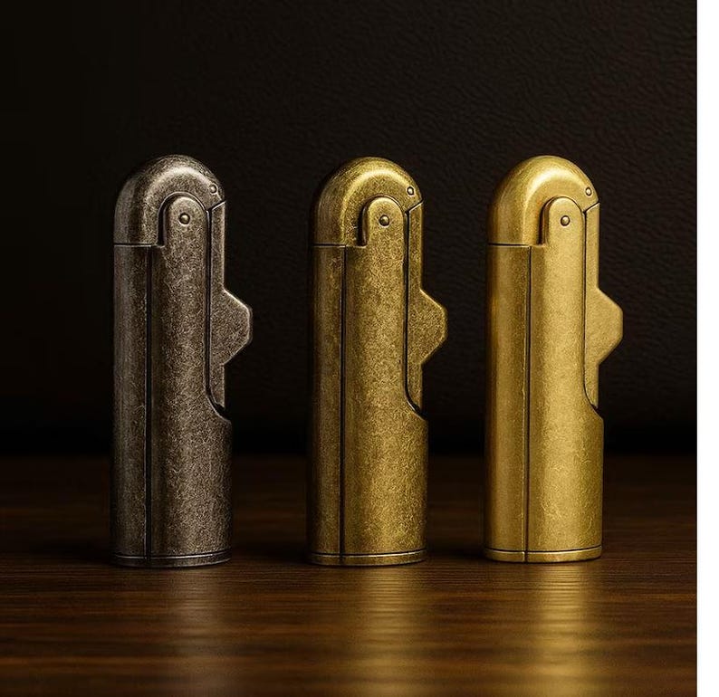 Peut inclure: Trois briquets de style vintage align&eacute;s, chacun avec une finition unique. Le premier est en bronze fonc&eacute; vieilli, le second en laiton chaud et le troisi&egrave;me en or brillant. Les briquets ont un corps rectangulaire avec un dessus incurv&eacute; et un levier lat&eacute;ral.
