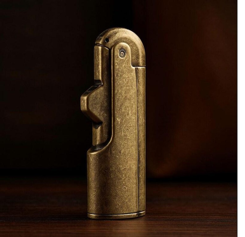 Peut inclure: Un briquet en laiton de style vintage avec un design unique. Le corps rectangulaire a un dessus arrondi et une surface textur&eacute;e. La finition en laiton lui donne un aspect antique. Le briquet est con&ccedil;u pour &ecirc;tre tenu &agrave; la main.