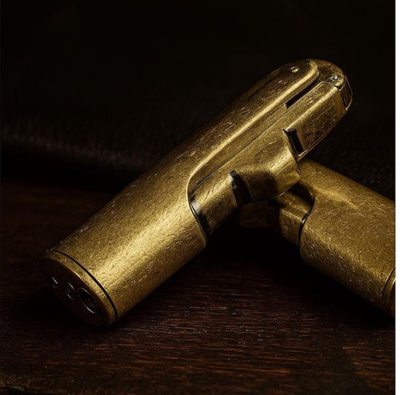 Peut inclure: Deux briquets antiques de couleur laiton sont pr&eacute;sent&eacute;s sur une surface en bois sombre. Les briquets ont une finition textur&eacute;e et une conception &agrave; charni&egrave;re. L'image est un gros plan, soulignant les d&eacute;tails du m&eacute;tal.
