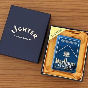 May include: A blue metal lighter with "Marlboro Lights" branding and a crest design, displayed in a navy blue box. The box is labelled "Lighter - High-Grade" in gold lettering. The lighter is in a black box with a yellow satin lining.