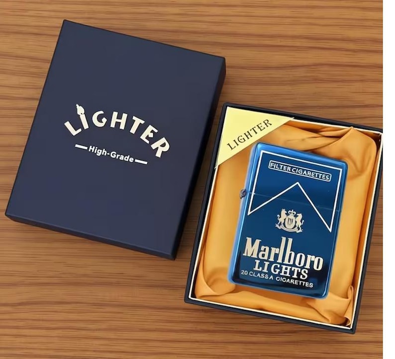 May include: A blue metal lighter with "Marlboro Lights" branding and a crest design, displayed in a navy blue box. The box is labelled "Lighter - High-Grade" in gold lettering. The lighter is in a black box with a yellow satin lining.