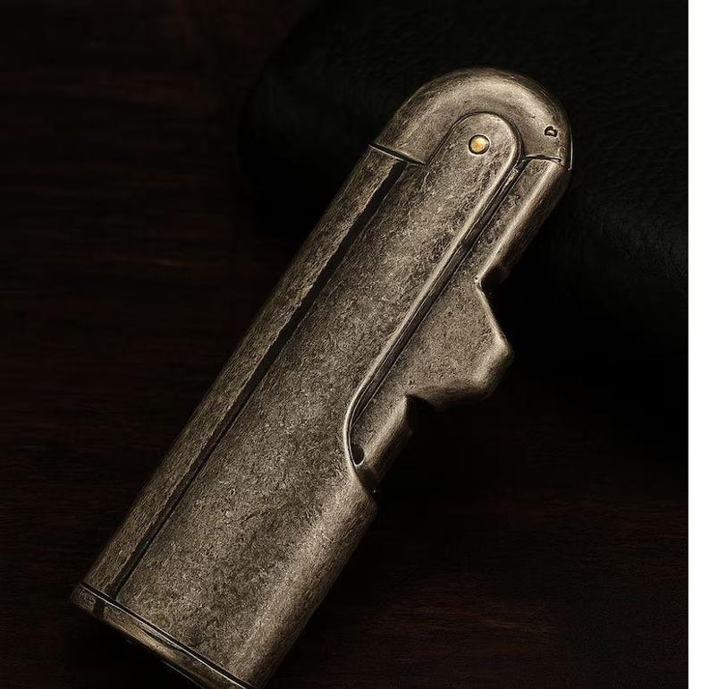 Peut inclure: Un briquet en m&eacute;tal de style vintage avec une finition vieillie et antique. Le corps rectangulaire a des bords arrondis et un dessus articul&eacute;. Un petit d&eacute;tail circulaire en laiton est visible pr&egrave;s du sommet. Le design sugg&egrave;re un objet de collection classique.