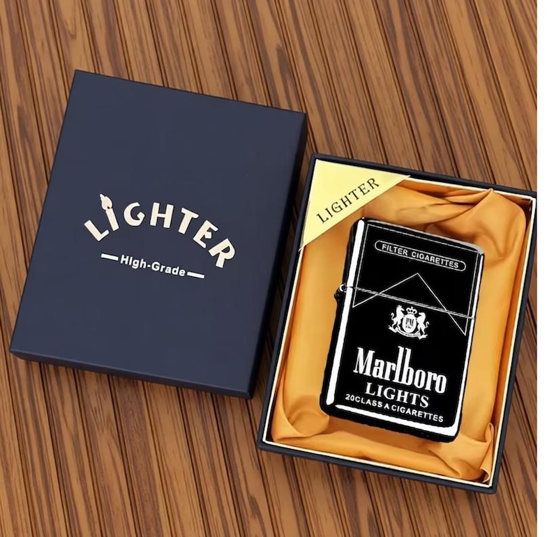 May include: A black and silver Marlboro Lights lighter in a navy blue gift box. The lighter features the Marlboro logo and text. The box is labelled "Lighter" and "High-Grade".