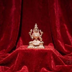 以下が含まれることがあります： 蓮の台座の上であぐらをかいて座っている、金色の金属製の神の小さな置物。このフィギュアには4本の腕があり、上の手には蓮のつぼみを持ち、下の手は手のひらを上に向けて開いたジェスチャーをしています。