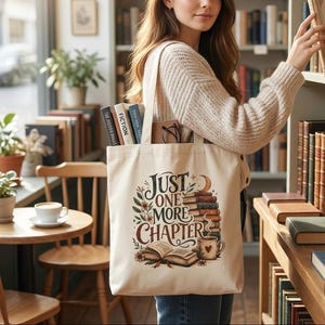 Peut inclure: Un sac fourre-tout crème avec le texte "Just One More Chapter" et des illustrations de livres, une tasse de café et des éléments floraux. Le sac est rempli de livres et de lunettes. La personne est dans une bibliothèque.