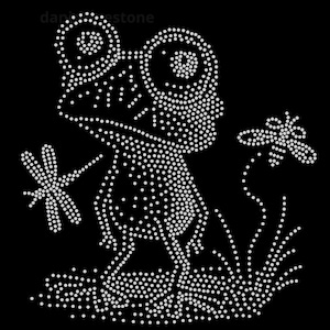 May include: A black iron-on transfer design featuring a frog with large eyes, a dragonfly, and a bee, all created with white rhinestones. The design includes the text dani-estone in the upper left corner, set against a solid black background.